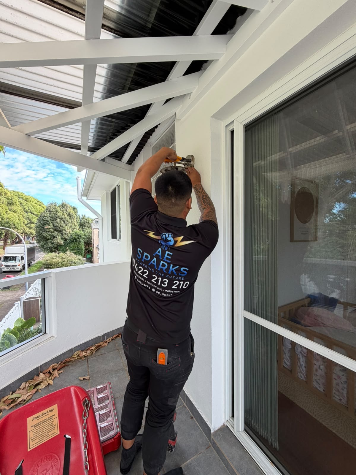 AE Sparks electrician in branded work shirt installing an outdoor light fitting